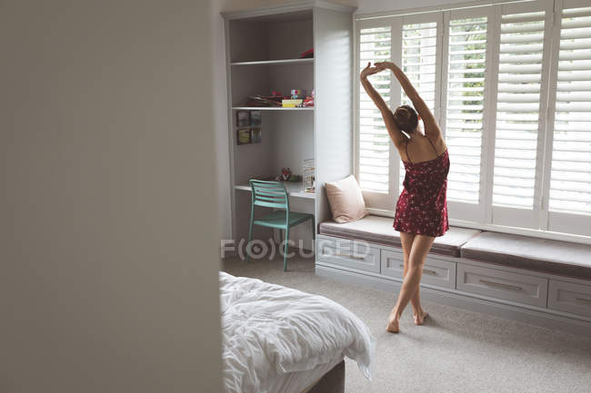 Vista trasera de la mujer caucásica estirando la mano por la mañana en el dormitorio en casa - foto de stock