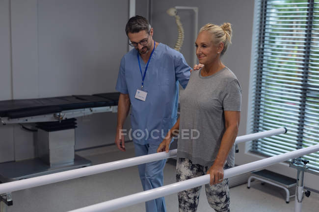 Visão frontal do fisioterapeuta masculino caucasiano ajudando paciente amputado feminino caucasiano a andar com barras paralelas no hospital — Fotografia de Stock