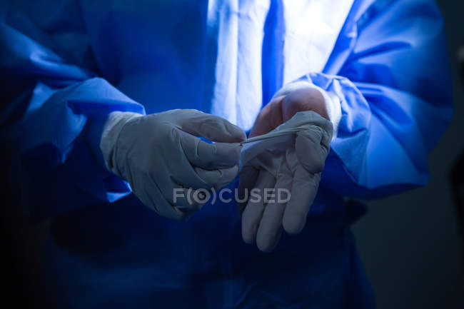 Secção média de cirurgiã a remover luvas cirúrgicas no teatro de operações — Fotografia de Stock