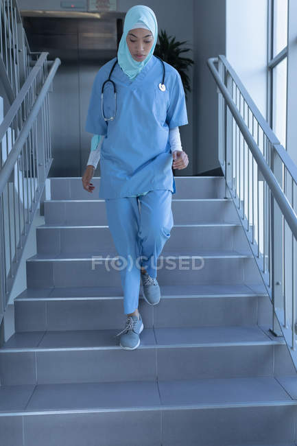 Frontansicht einer jungen Ärztin mit gemischter Rasse im Hijab, die im Krankenhaus die Treppe hinuntergeht — Stockfoto