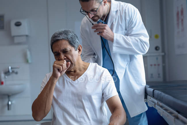 Front view of Caucasian male doctor examining senior mixed-race patient with stethoscope in hospital — Stock Photo