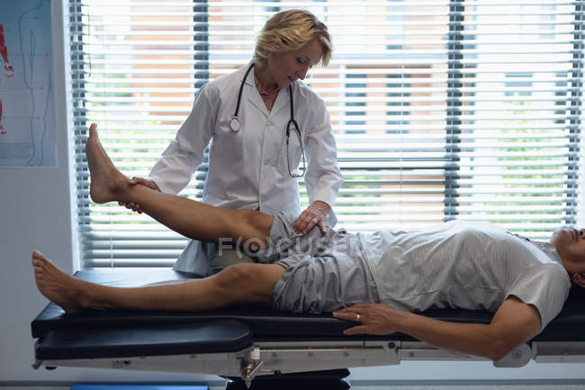 Front view of mature Caucasian female doctor examining senior mixed-race male patient back in hospital — Stock Photo