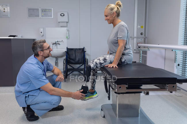 Vista lateral del fisioterapeuta masculino caucásico ajustando la pierna protésica de la paciente femenina en el hospital - foto de stock