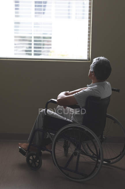 Side view of disabled mixed race patient in wheelchair looking through window in the ward at hospital — Stock Photo