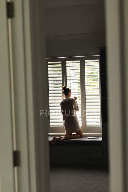 Rear view of Caucasian woman looking through window at home — Stock Photo