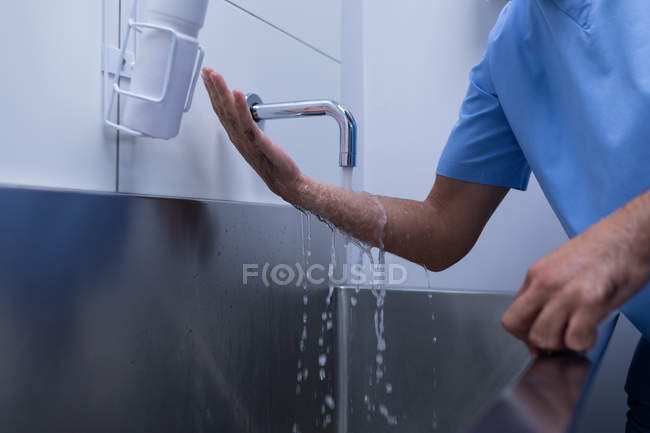 Sección media del cirujano masculino lavándose las manos con jabón en el lavabo en el hospital - foto de stock