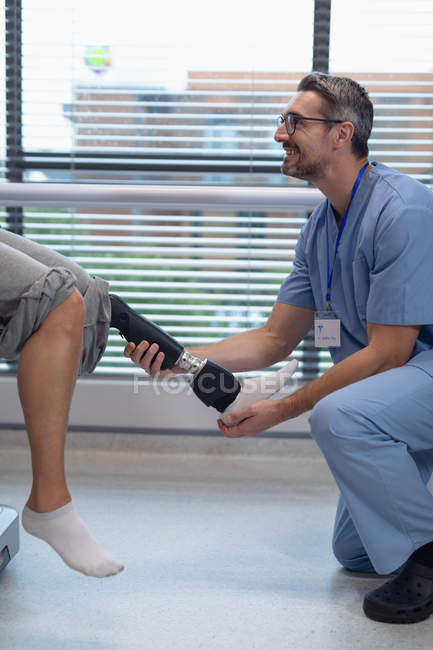 Side view of happy Caucasian male physiotherapist adjusting prosthetic leg of female patient in hospital — Stock Photo