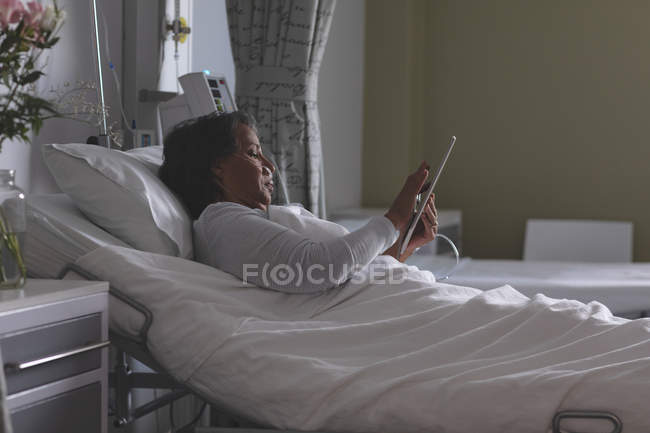 Side view of pretty mixed-race female patient using digital tablet in the ward at hospital. — Stock Photo