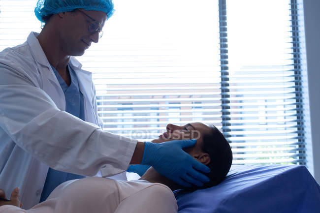 Vista lateral del guapo cirujano caucásico de mediana edad examinando a una hermosa paciente caucásica en el hospital - foto de stock