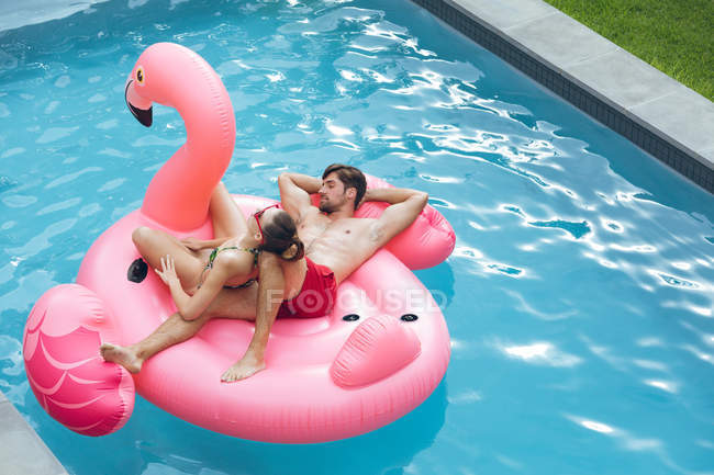 Vista alta de pareja caucásica durmiendo juntos en un tubo inflable en la piscina en el patio trasero - foto de stock