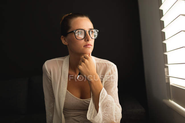 Vista frontale della donna caucasica guardando attraverso la finestra mentre seduto su un divano in soggiorno a casa — Foto stock