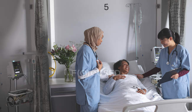 Вид спереду на різноманітних жінок-лікарів, що взаємодіють зі зрілими пацієнтами змішаної раси у лікарні. Жіночий пацієнт виглядає полегшеним . — стокове фото