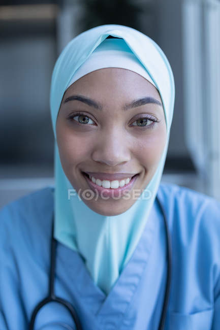 Portrait of mixed race female doctor in hijab sitting on staircase in hospital — Stock Photo