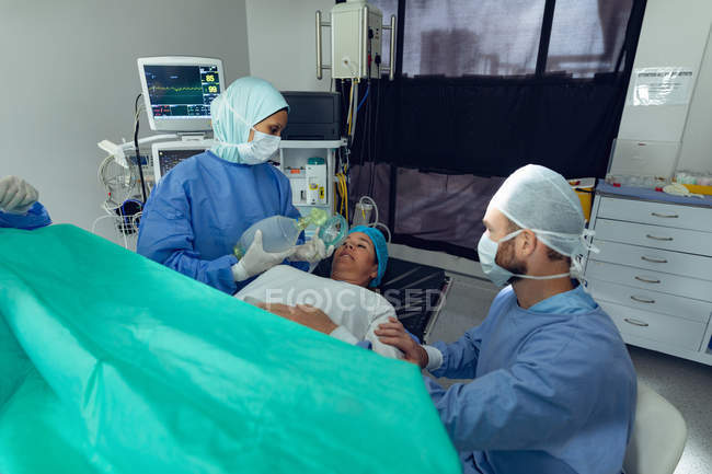 Vue en angle élevé de l'homme caucasien réconfortant la femme enceinte pendant le travail tandis que le médecin féminin métis utilise un respirateur sur le patient dans le théâtre d'opération à l'hôpital — Photo de stock