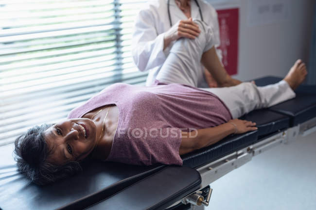 Vista de ángulo alto de la doctora caucásica examinando la pierna de una paciente de raza mixta en el hospital - foto de stock