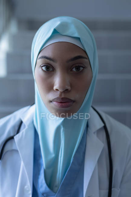 Portrait of mixed-race female doctor in hijab sitting on staircase in the hospital — Stock Photo