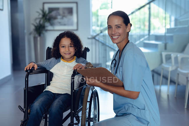 Porträt einer kaukasischen Ärztin, die mit einem behinderten Mischlingsjungen auf dem Krankenhausflur lächelt — Stockfoto