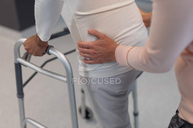 Low section of female physiotherapist helping mixed-race female patient walk with walker in the hospital — Stock Photo