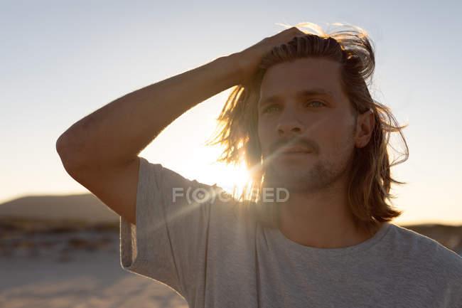Front view of thoughtful young Caucasian man with hand on head looking away on the beach — Stock Photo