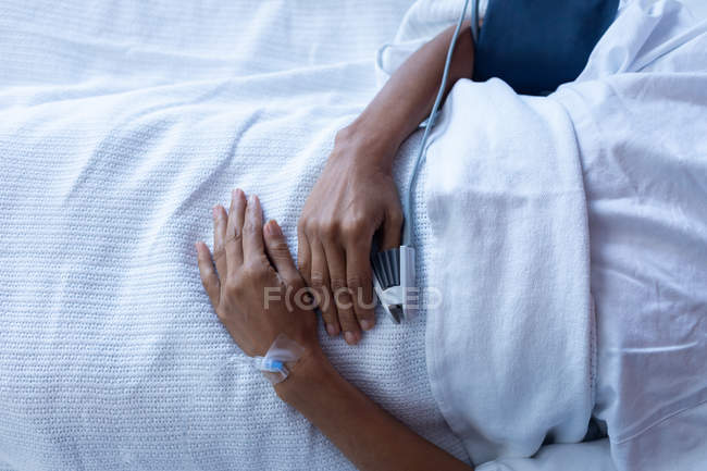 Mid section of female patient lying on bed in the ward at hospital. She is getting IV therapy and pulse oximetry is measuring her blood. — Stock Photo