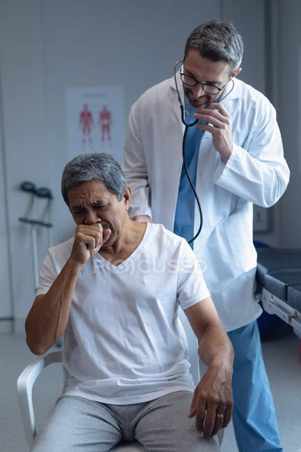 Первый взгляд врача-кавказца, осматривающего пожилого пациента смешанной расы со стетоскопом в больнице — стоковое фото