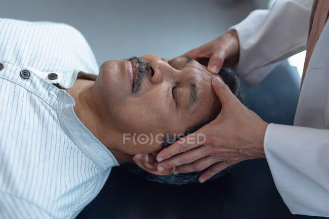 Seção intermediária do médico examinando o paciente mestiço sênior do sexo masculino no hospital — Fotografia de Stock