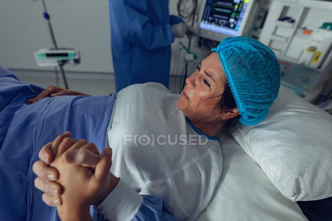 Vista trasera del hombre que consuela a la mujer embarazada durante el parto en el quirófano en el hospital - foto de stock