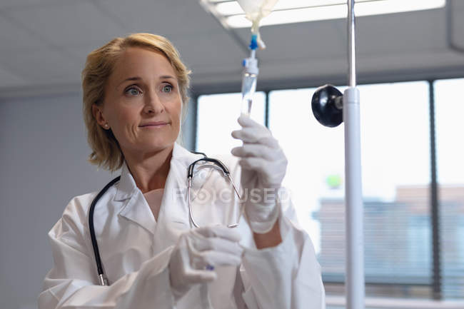 Vista frontal del médico femenino caucásico ajustando goteo intravenoso en el hospital - foto de stock