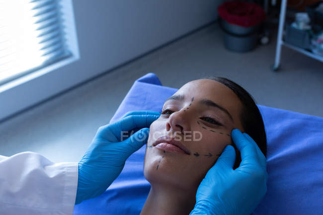 Close up of male surgeon examining pretty Caucasian female patient face in hospital. — Stock Photo