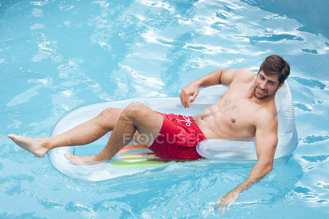Vista alta del hombre caucásico feliz que relaja en una melodía inflable en la piscina - foto de stock