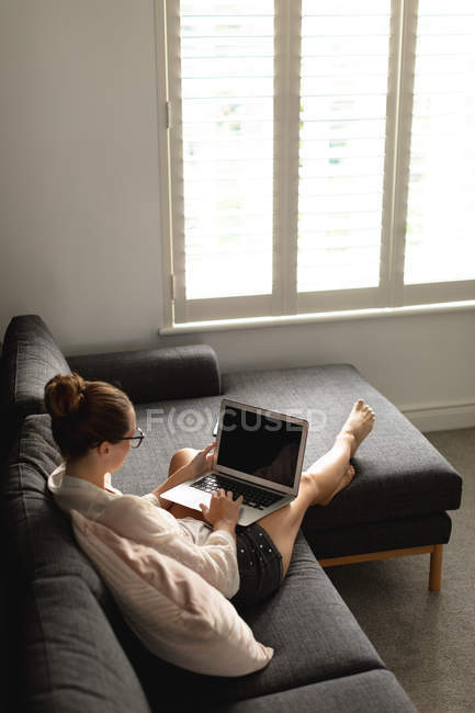 Высокий вид на кавказскую женщину с помощью ноутбука на диване в гостиной на дому — стоковое фото