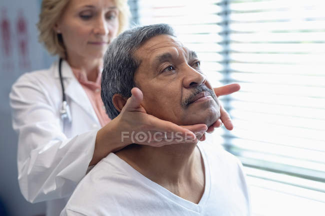 Vista frontal do médico branco do sexo feminino examinando pescoço mestiço do paciente masculino no hospital — Fotografia de Stock
