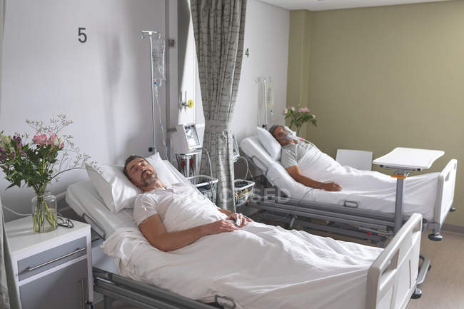 Вид збоку на різних пацієнтів чоловічої статі, які сплять у ліжку в палаті в лікарні — стокове фото