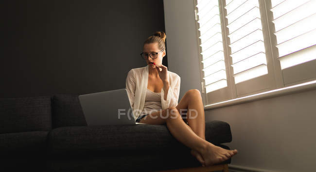 Front view of Caucasian woman using laptop on a sofa in living room at home — Stock Photo