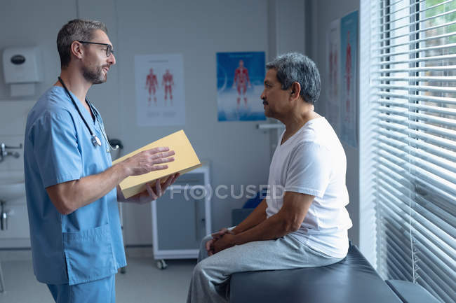 Вид сбоку красивого белого хирурга со стетоскопом вокруг шеи, взаимодействующего с пациентом в больнице — стоковое фото