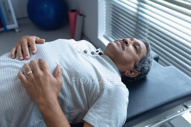 Вид збоку на старшу змішану расу чоловічий пацієнт лежить на огляді ліжка в лікарні — стокове фото
