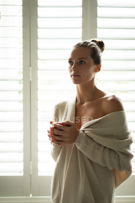 Vista frontale della donna caucasica con tazza di caffè guardando lontano a casa — Foto stock