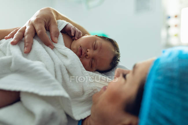 Vista lateral de la madre sosteniendo a su bebé recién nacido en quirófano en el hospital - foto de stock
