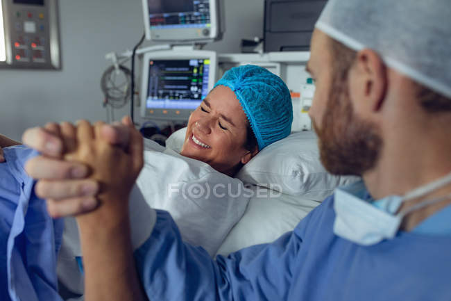 Vista lateral del hombre caucásico reconfortando a la mujer embarazada durante el parto en el quirófano en el hospital - foto de stock