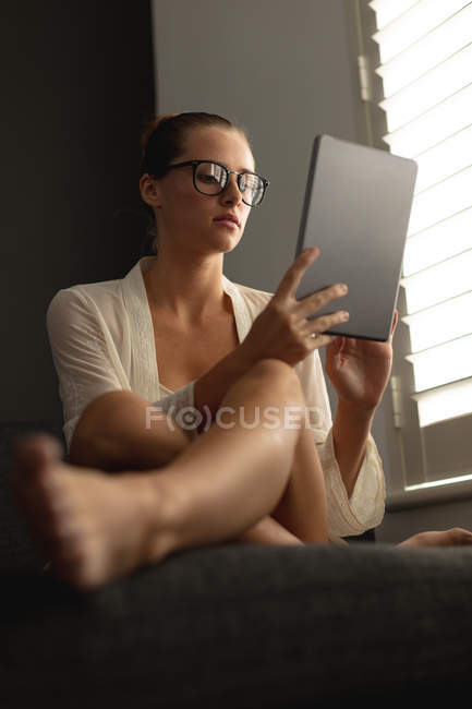 Вид збоку кавказька жінка з використанням цифрової планшета на дивані у вітальні будинку — стокове фото
