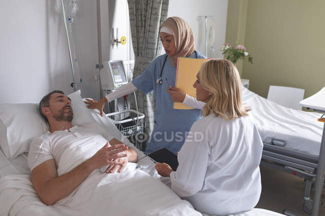 Вид збоку різних жінок-медиків, що взаємодіють з Кавказького чоловічого пацієнта в палаті у лікарні — стокове фото