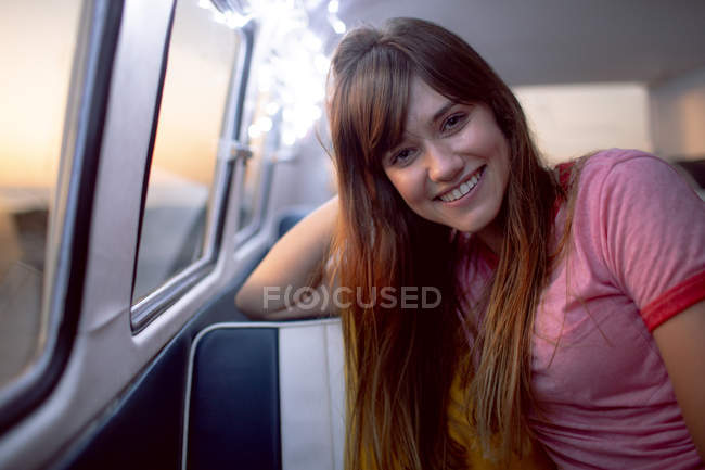 Вид спереди счастливой белой женщины, смотрящей в камеру, сидящей в фургоне на пляже — стоковое фото