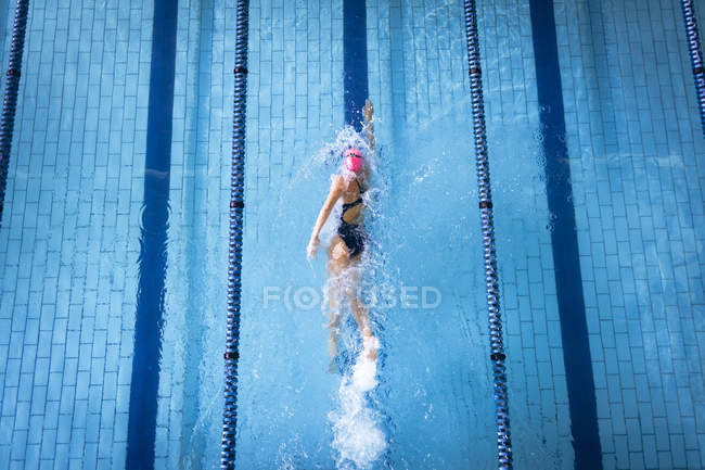 Vista de alto ângulo de uma mulher caucasiana vestindo um maiô e um boné de banho rosa fazendo freestyle acidente vascular cerebral na piscina — Fotografia de Stock