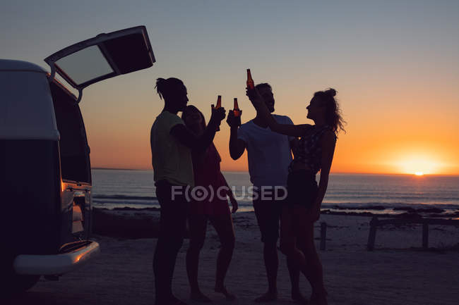 Vista laterale di gruppo di diversi amici che hanno birra vicino camper durante il tramonto — Foto stock