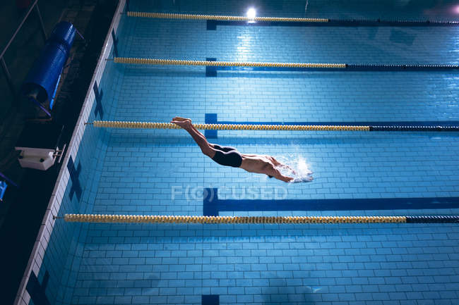 High angle view of a male Caucasian swimmer wearing a white swimming cap diving in the swimming pool — Stock Photo
