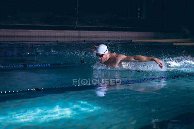Vista laterale di un nuotatore caucasico maschio che tiene gli occhiali sul suo berretto bianco mentre si trova in piscina — Foto stock
