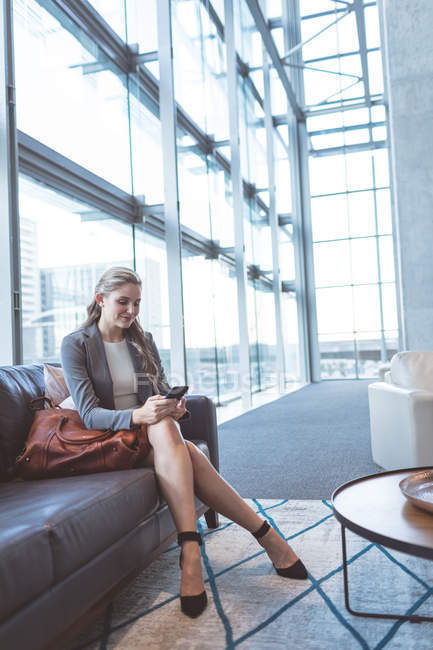 Seitenansicht der schönen Geschäftsfrau mit dem Handy auf dem Sofa in der Lobby im modernen Büro — Stockfoto