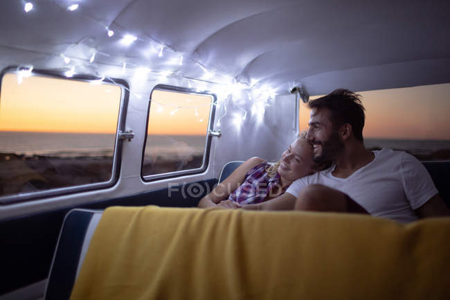 Front view of happy Caucasian couple sitting together in a camper van at beach during sunset — Stock Photo