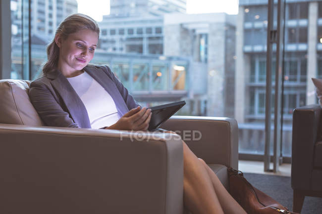 Vista frontal de empresária trabalhando em tablet digital no sofá no lobby no escritório moderno — Fotografia de Stock