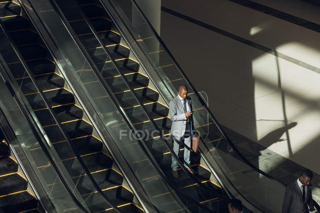 Vista aérea del ejecutivo afroamericano maduro usando escaleras mecánicas en la oficina moderna - foto de stock